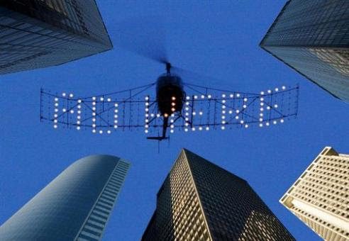 A helicopter with lights flying over some buildings.